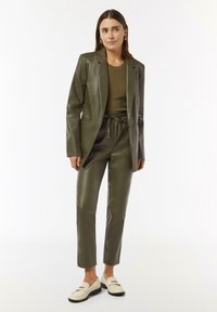 Olivengrünes Blazer- und Hosen-Set aus Kunstleder, mit einem strukturierten Pullover darunter. Abgerundet mit cremefarbenen Slippern. Glatter, taillierter Schnitt.