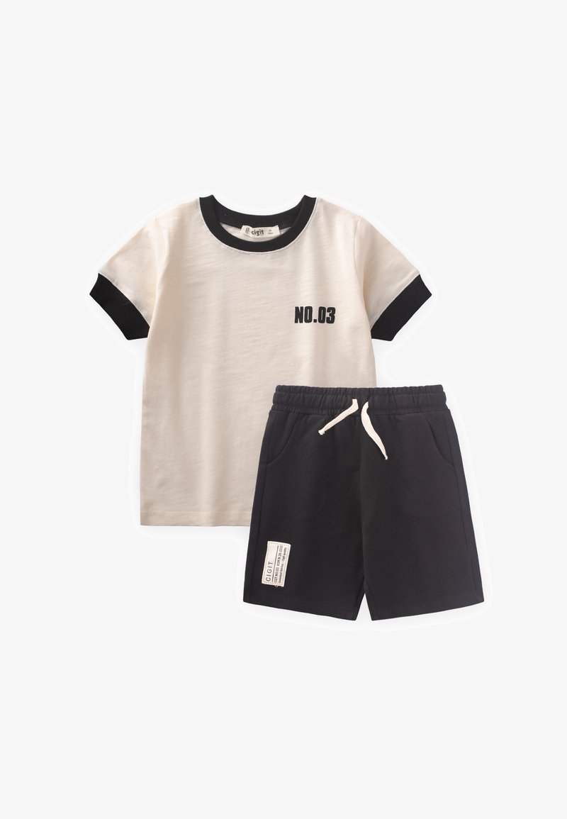 Kaheosaline riietus, mis sisaldab kreemikat T-särki mustade detailidega ja prinditud "NO.03", koos navü siniste lühikesed pükstega, millel on valge silt ja nööri tõmblukk.