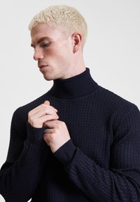 Maglione a collo alto lavorato a maglia blu navy, con un motivo testurizzato, polsini a costine e una vestibilità aderente che mette in risalto il collo e le maniche.