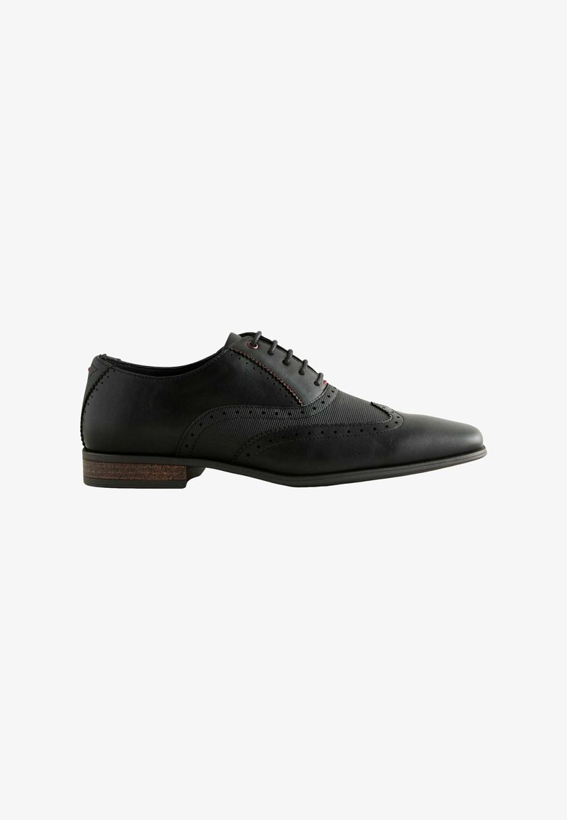 Chaussure habillée en cuir noir avec un bout pointu, des perforations décoratives, des panneaux texturés et un talon en bois. Les lacets et les coutures rouges rehaussent le design.
