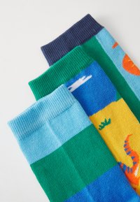 Trois paires de chaussettes aux couleurs variées : marine, verte, bleu clair, avec des motifs incluant des montagnes et des créatures marines. Tricot texturé.