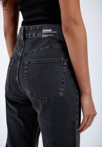 Black denim jeans featuring a high waist, five-pocket design, and a visible brand label on the back with a textured finish.