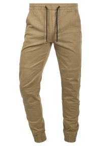 Kaki-färgade tapered joggerbyxor med elastisk midja, svarta dragsnören, sydda knädetaljer och elastiska muddar vid anklarna.