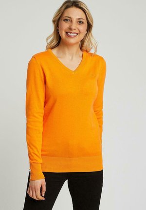Pull à col en V orange en tissu lisse, avec des manches longues et des accents de boutons aux poignets. Design ajusté avec ourlet côtelé.