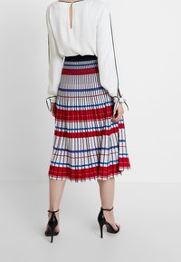 Blauw, rood en wit gestreepte geplooide rok; kniehoog met uitgesproken verticale lijnen. Draagt een witte blouse en zwarte sandalen met hoge hakken.