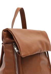 Mochila de cuero marrón con un acabado texturizado, tapa plegable, cremallera lateral y un asa superior para un fácil transporte.