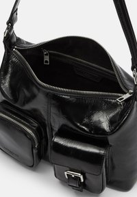 Czarna skórzana torebka charakteryzuje się błyszczącym wykończeniem, podwójnymi komorami na zamek, dwoma kieszeniami z przodu na zamki oraz paskiem na ramię.