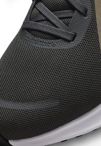 Gros plan sur une chaussure de sport en mesh noir avec des superpositions synthétiques texturées et des lacets noirs sur une semelle blanche.
