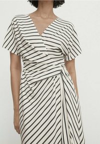 Randig omslagklänning i creme och marinblå; har korta ärmar, en djup V-ringning och ett knytband i midjan för en figurnära silhuett.