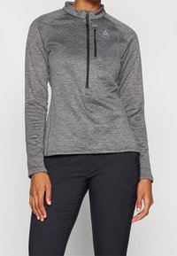 Grå sportig pullover med dragkedja i halsen, långa ärmar och en kroppsnära silhuett. Har en subtil textur och en liten logotyp på bröstet.