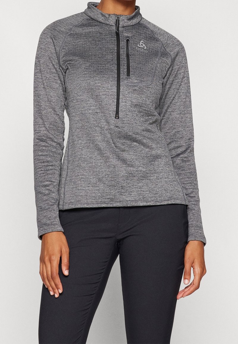 Grå sportig pullover med dragkedja i halsen, långa ärmar och en kroppsnära silhuett. Har en subtil textur och en liten logotyp på bröstet.