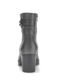 Zwarte leren enkellaars met blokhak, ritssluiting en een verstelbare banddetail. Gladde textuur en gestikte accenten.