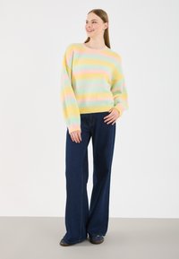 Pulover cu dungi pastelate, din tricot moale, cu nuanțe de galben, roz, albastru și verde. Se asortează cu blugi largi, de culoare albastru închis.
