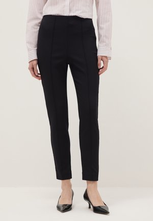 Woman wearing slim-fit black ankle pants, a tucked-in striped long-sleeve shirt, and black pointed-toe heels standing against a neutral background.