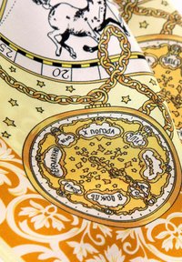 Geel zijden stof met ingewikkelde illustraties, waaronder een kettingontwerp, sterren en astrological symbolen op een gemusterde achtergrond.