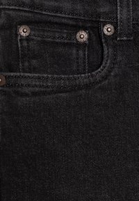 Černá denimbová tkanina s hladkým povrchem, obsahující malou přední kapsičku, kovové nýty a kontrastní švy.