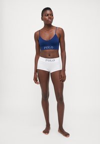 Tumši zils bralets un baltas hipster šortus, abi ar kontrastējošu "POLO" logo. Mīksta auduma, vienkāršs dizains, pieguloša siluets.