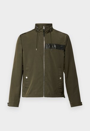 Oliwkowa kurtka z wysokim kołnierzem, z zamkiem z przodu i dwiema kieszeniami po bokach. Posiada czarny panel z logo na klatce piersiowej oraz regulowane sznurki.