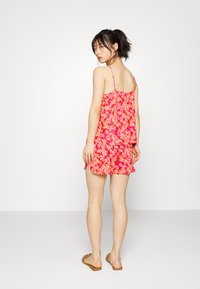 Vestido floral em rosa brilhante com padrões de folhas amarelas e laranjas, apresentando alças finas e uma bainha em camadas com rufos.