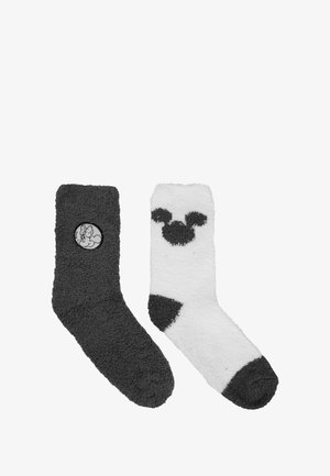 Two pairs of fuzzy socks: one gray with a circular black logo, the other white with a black Mickey Mouse pattern and accents.