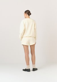 Kremowy zestaw bluzy i szortów wykonany z miękkiego materiału, charakteryzujący się luźnym krojem. Noszony z czarnymi mokasynami i jasnymi skarpetami.