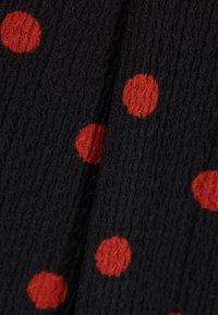 Mustavärinen kuitukangas, jossa on epäsäännöllisiä punaisia pilkkuja. Lähikuva, jossa korostuvat värit ja pinnan yksityiskohdat.