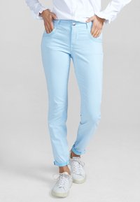 Ljusblå slim-fit jeans med framfickor, knappstängning och uppvikta fållar, kombinerat med vita sneakers. Slät tygstruktur.