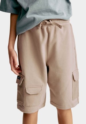 Pantalones cortos de carga beige con bolsillos laterales, fabricados con material suave. Presentan una cinturilla ajustable con cordón y un detalle de costura mínima.
