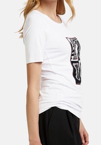 T-shirt bianco a maniche corte con una stampa grafica audace nera e argENTO sulla parte anteriore, realizzato in morbido cotone e con una vestibilità rilassata.