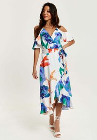 White floral dress featuring colorful blue and orange patterns, v-neck with ruffled sleeves, wrap design, and ankle-length asymmetric hem.
