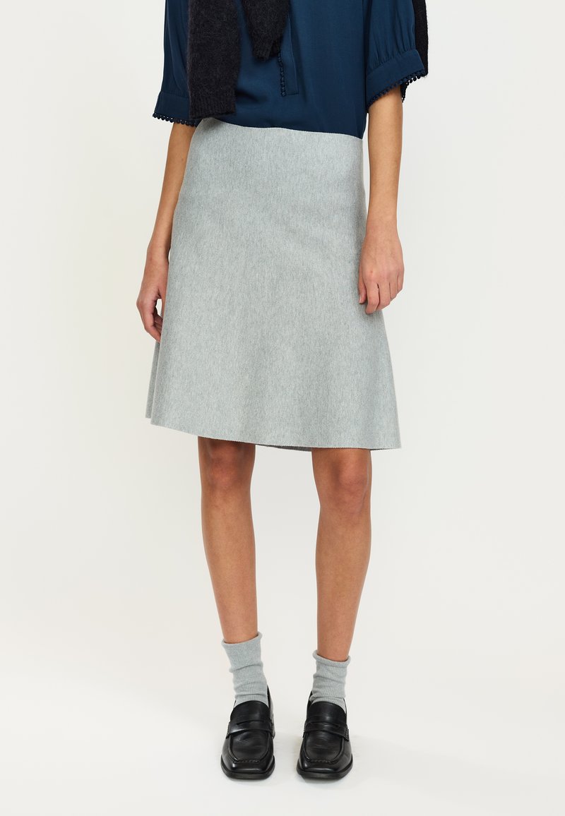 Gonna svasata grigia in tessuto morbido con una texture sottile, abbinata a una blusa blu navy e mocassini neri, accessoriata con calzini grigi.