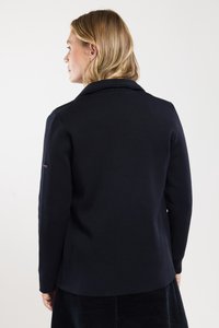 Blazer texturé bleu marine avec un col, des manches longues et une coupe cintrée. Détail notable : petit logo sur la manche gauche.