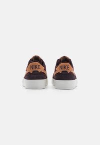 Adidași Nike cu un superior din suede în nuanțe de maron și bej, talpă albă și logo-ul proeminent al mărcii pe spate. Fără embellishments suplimentare.