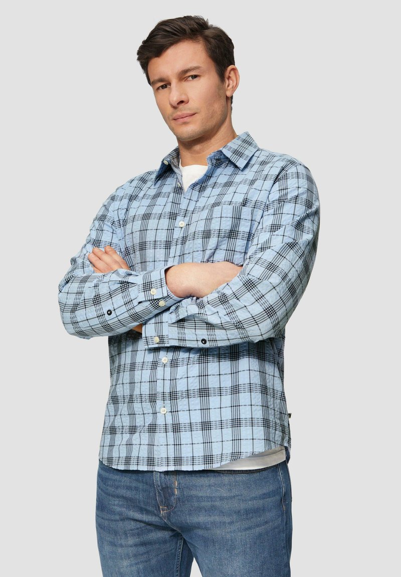 Blauw geruite shirt met zwart-wit ruitpatroon, knoopsluiting aan de voorkant, lange mouwen en een borstzak, gecombineerd met blauwe spijkerbroek.