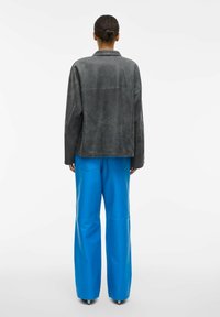 Hall textuuriga seemisnahast jakk lõdva istuvusega, tagumine yoke detail ja laiad sinised püksid läikiva tekstuuri ja suurte taskutega. Lihtne, kaasaegne disain.