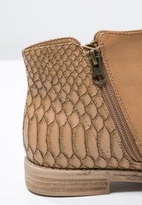 Kohokuvioitu käärmeennahkakuosiset vaaleanruskeat nilkkasaappaat, joissa on sivuvetoketju ja sileät nahkakorostukset.