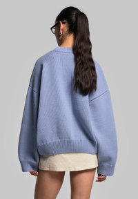 Maglione di maglia a vestibilità ampia in azzurro chiaro, con maniche larghe, orlo a coste e tessuto testurizzato. Indossato sopra una gonna beige.