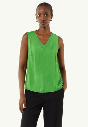 Green sleeveless top in smooth fabric, featuring a V-neckline, subtle pocket detail, and relaxed fit, paired with black trousers.