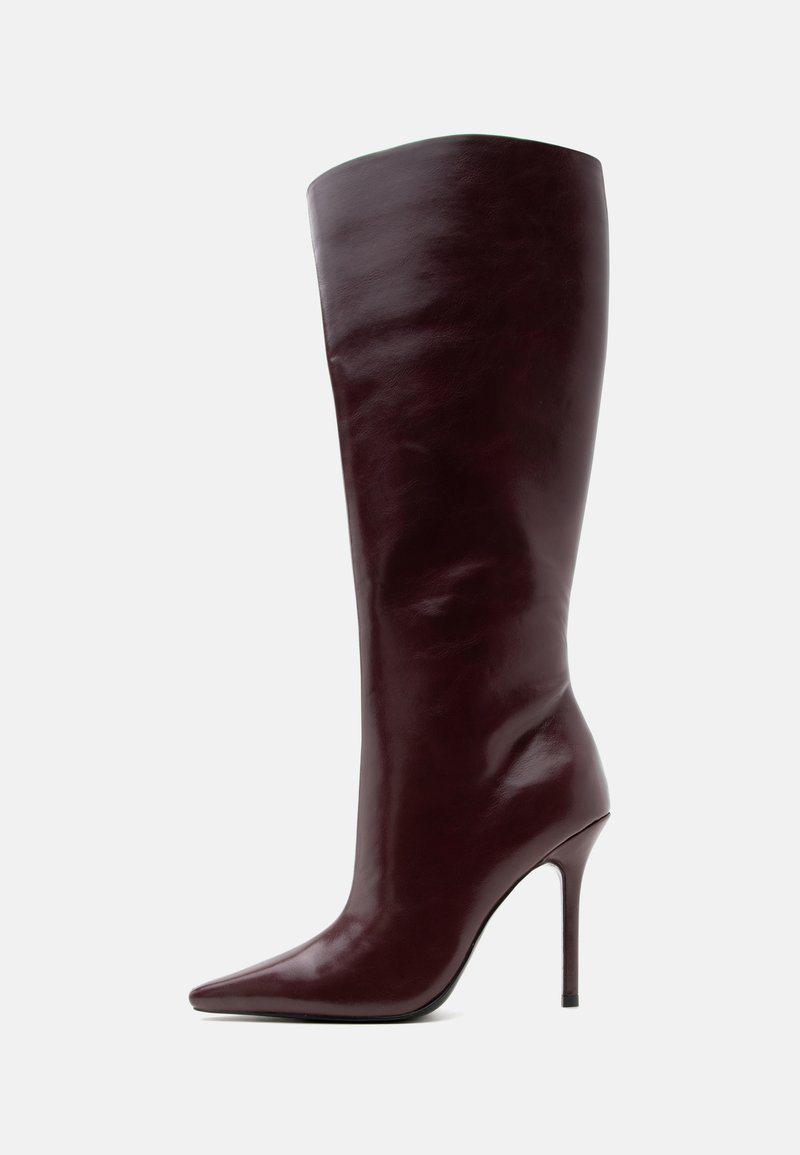 Botte en cuir marron foncé montant jusqu’au genou avec bout pointu et talon haut fin sur fond clair.