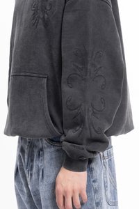 Temno siva dukserica s teksturirano cvetno vezenje na rokavih, kenguru žepom in rebrastimi manšetami, v kombinaciji z visokim pasom jeans.