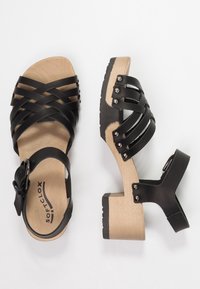 Zwarte sandalen met bandjes, een houten blokhak, open teenontwerp, verstelbare enkelriem en decoratieve zilveren studs aan de zijkanten.