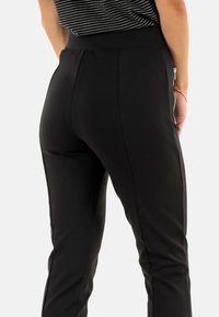 Pantaloni neri elasticizzati con vita alta, dotati di tasche laterali con zip e una vestibilità sartoriale, texture liscia e senza motivi visibili.