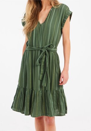 Robe verte à motif avec un décolleté en V, des manches courtes et une ceinture à nouer. Elle présente des rayures verticales avec des points et un ourlet volé.