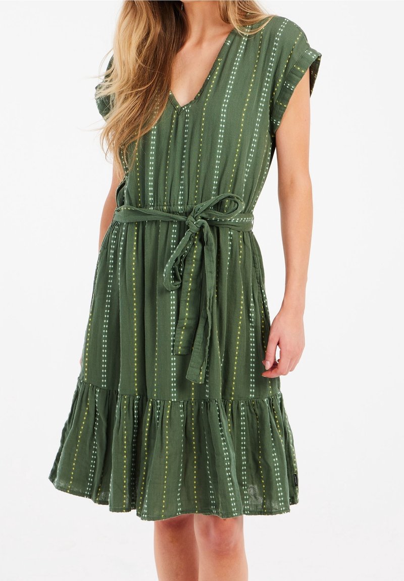 Grünes gemustertes Kleid mit V-Ausschnitt, kurzen Ärmeln und einem Bindegürtel. Das Kleid hat senkrechte Streifen mit Punkten und einen rüschenbesetzten Saum.