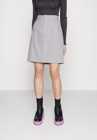 Jupe évasée grise en tissu texturé avec des plis à l'avant. Associée à des bottines à plateforme noires avec des semelles violettes.