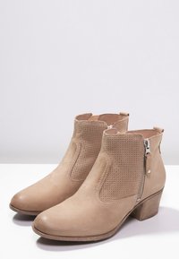 Beige nilkkurit, jotka on valmistettu sileästä mokasta, ja niissä on kudotut paneelit, sivuvetoketjut ja pinottu korko. Pyöreä kärki ja sileä pinta.