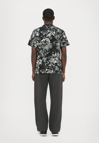 Μαύρο και γκρι πουκάμισο με λουλουδάτο μοτίβο και κοντά μανίκια, συνδυασμένο με γκρι παντελόνι σε φαρδιά γραμμή και μαύρα αθλητικά παπούτσια.