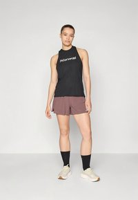 Top esportivo preto sem mangas com texto branco "Normal", combinado com calções malva e meias pretas. Modelo usa ténis claros.