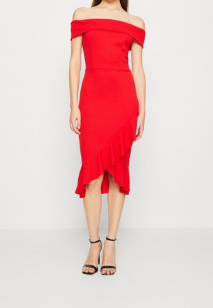 Woman wearing a red off-shoulder midi dress with asymmetrical ruffle hem paired with black ankle-strap high-heeled sandals.