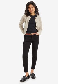 Krémszínű, kötött kártyigán, kerek nyakkal és gombokkal, fekete pólóval, fekete, slim-fit farmernadrággal és fekete mokaszinnal párosítva. Barna öv kiemeli az összeállítást.
